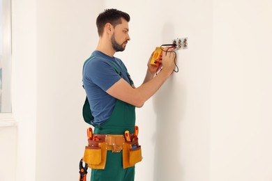 Electrician in uniform with tester checking voltage indoors