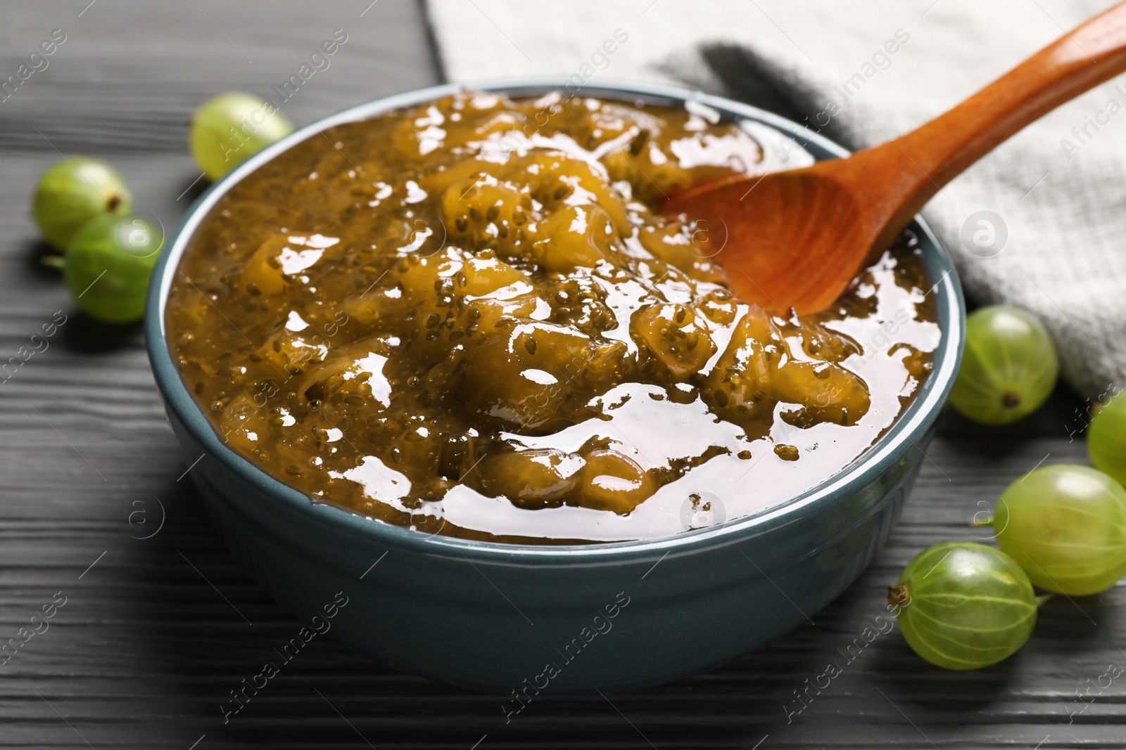 Photo of Delicious gooseberry jam with spoon and fresh berries on grey wooden table, closeup