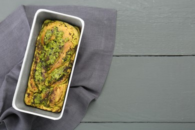 Photo of Freshly baked pesto bread in loaf pan on grey wooden table, top view. Space for text