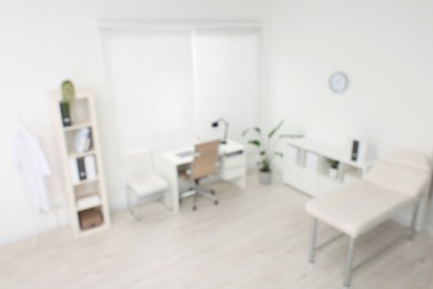 Photo of Blurred view of modern medical office with doctor's workplace and examination table in clinic