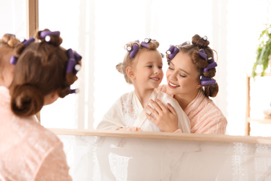 Happy mother and daughter with curlers near mirror in bathroom
