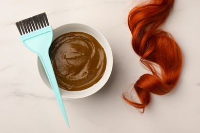 Photo of Bowl of henna cream, brush and red strand on white marble table, flat lay. Natural hair coloring