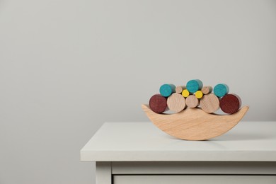 Photo of Wooden balance toy on chest of drawers near light grey wall, space for text. Children's development