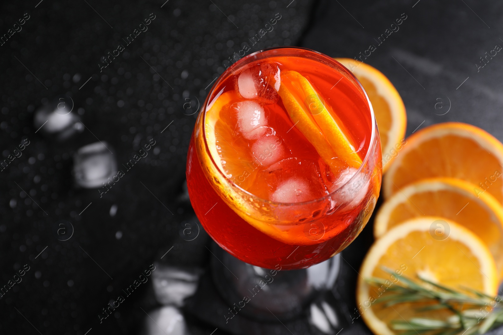 Photo of Glass of tasty Aperol spritz cocktail with orange slices and ice cubes on black table, above view