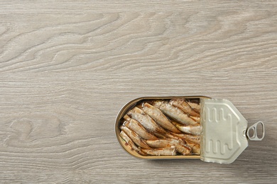 Open tin can of sprats on wooden background, top view. Space for text