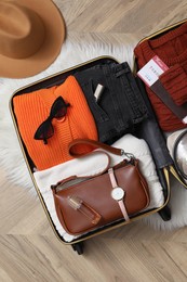 Open suitcase with folded clothes and accessories on floor, flat lay