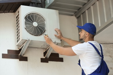 Professional technician maintaining modern air conditioner outdoors