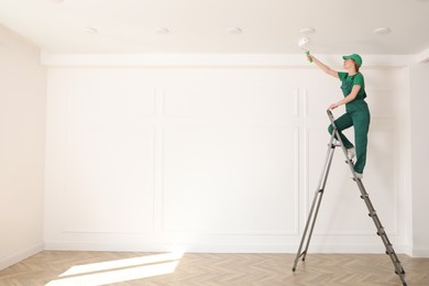 Photo of Worker painting ceiling with white dye indoors, space for text