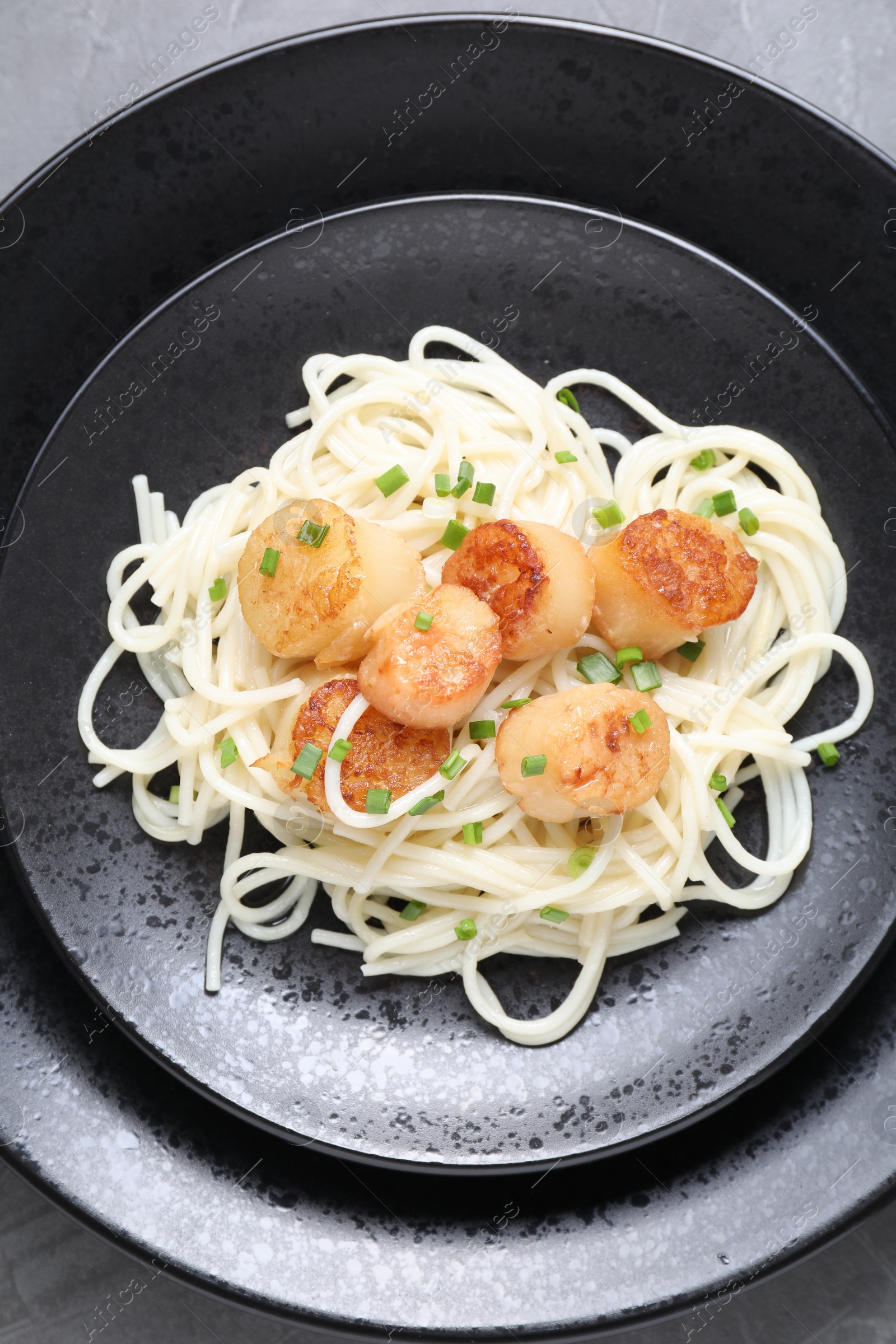 Photo of Delicious scallop pasta with green onion on grey table, top view