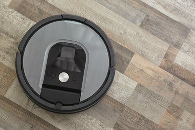 Modern robotic vacuum cleaner on wooden floor, top view. Space for text