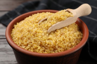 Photo of Bowl and scoop with raw bulgur on table, closeup