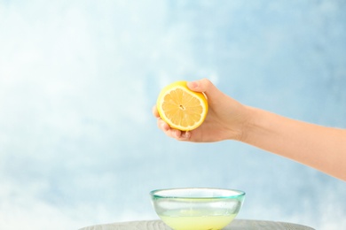 Photo of Young woman squeezing lemon juice into bowl on color background