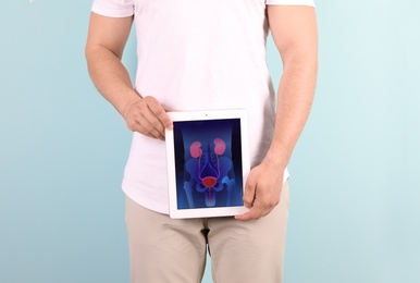Young man holding tablet with urinary system on screen against color background