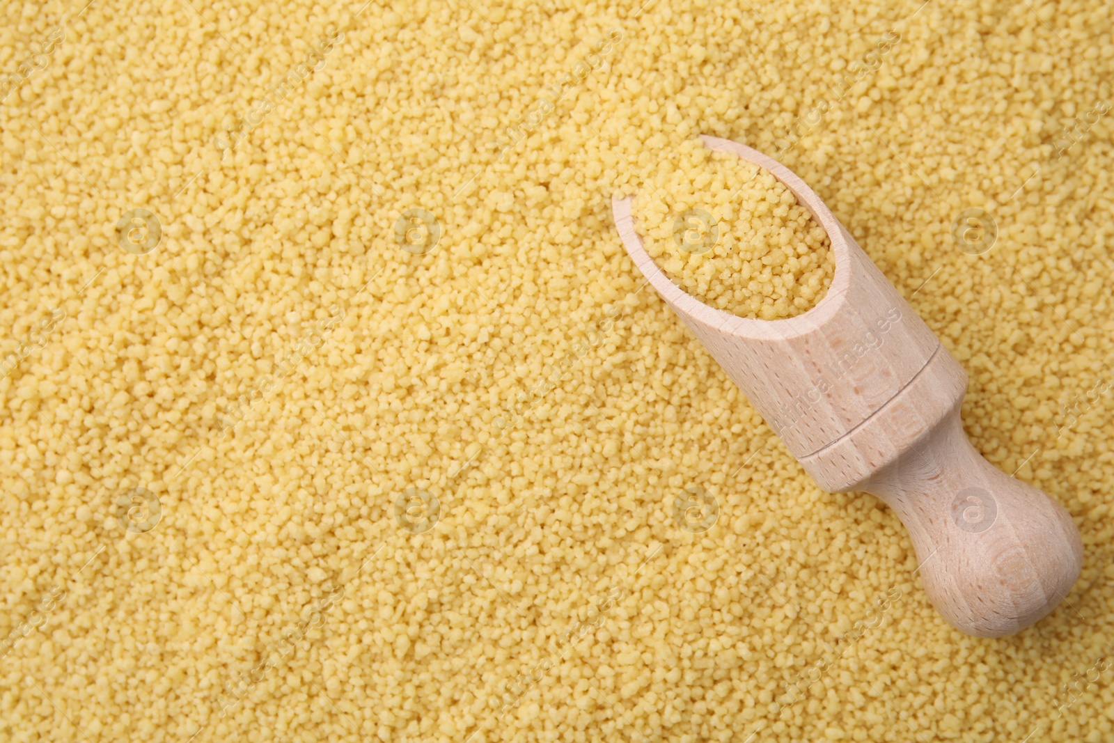 Photo of Wooden scoop and uncooked organic couscous as background, top view. Space for text