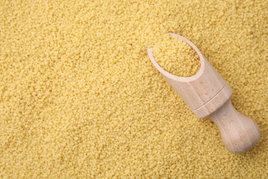 Wooden scoop and uncooked organic couscous as background, top view. Space for text