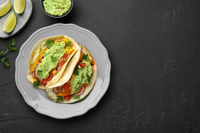 Delicious tacos with guacamole and vegetables served on black table, flat lay. Space for text