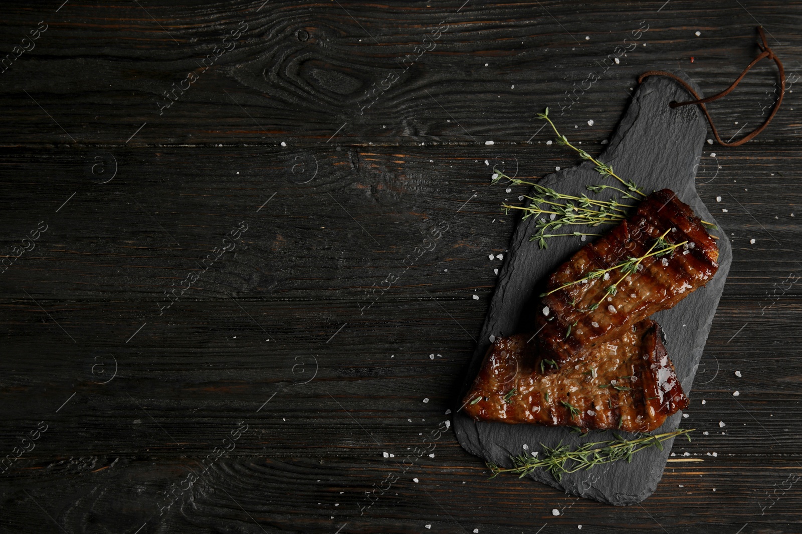 Photo of Board with grilled meat on wooden table, top view. Space for text