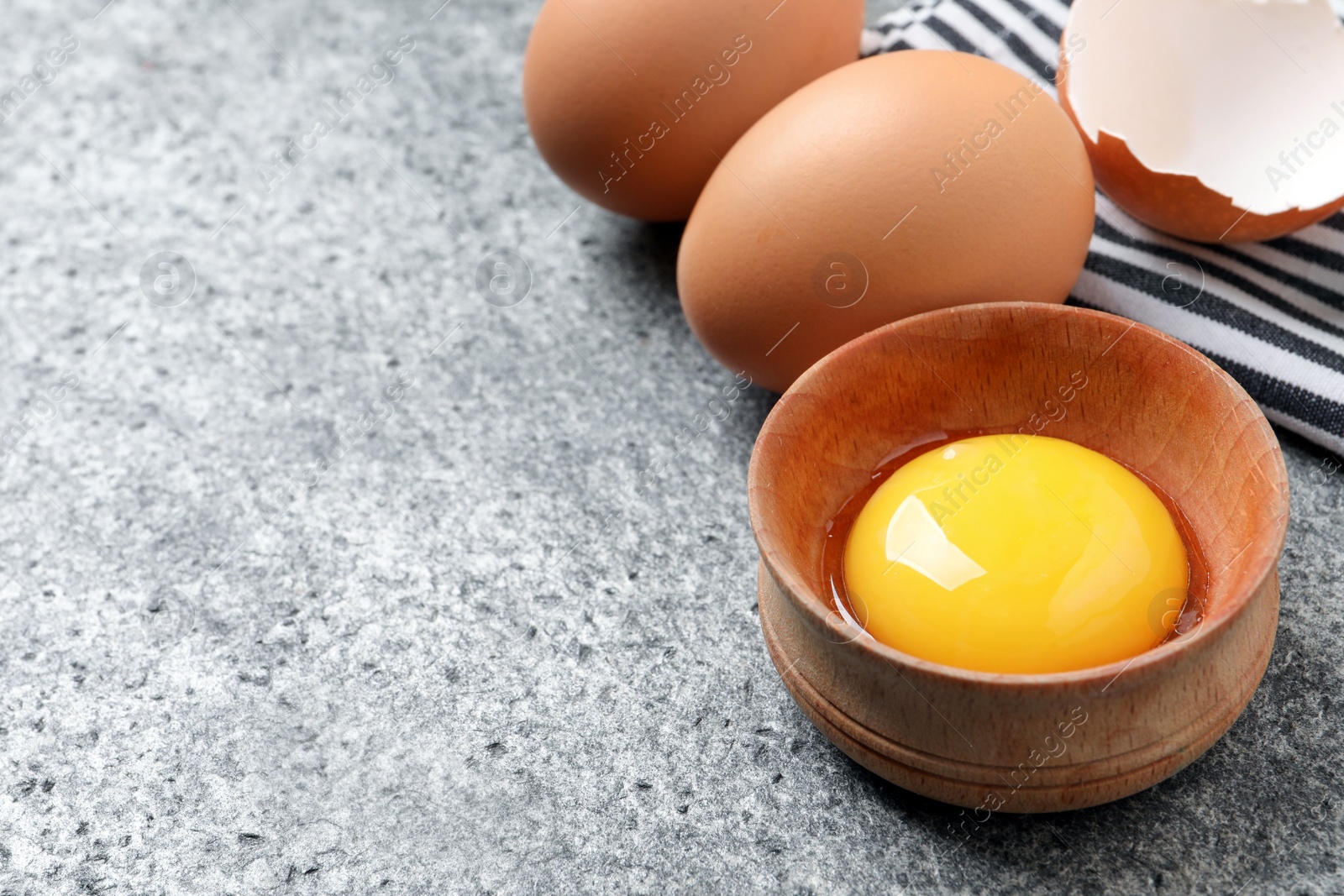 Photo of Raw chicken eggs and bowl with yolk on grey table, closeup, space for text