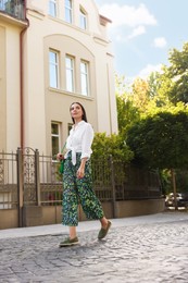 Beautiful young woman in stylish outfit walking on city street