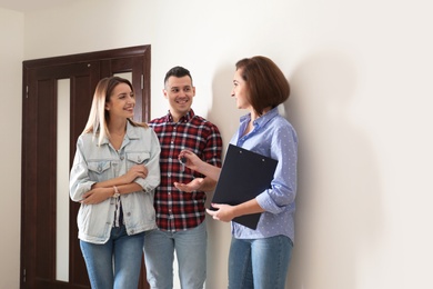 Real estate agent giving apartment keys to young couple indoors
