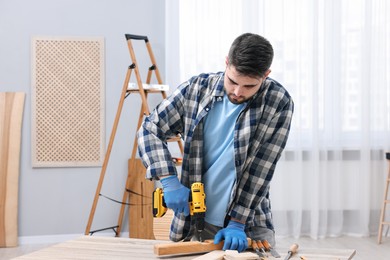 Young handyman working with electric drill at table in workshop