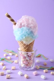 Photo of Sweet cotton candy in waffle cone and marshmallows on purple background