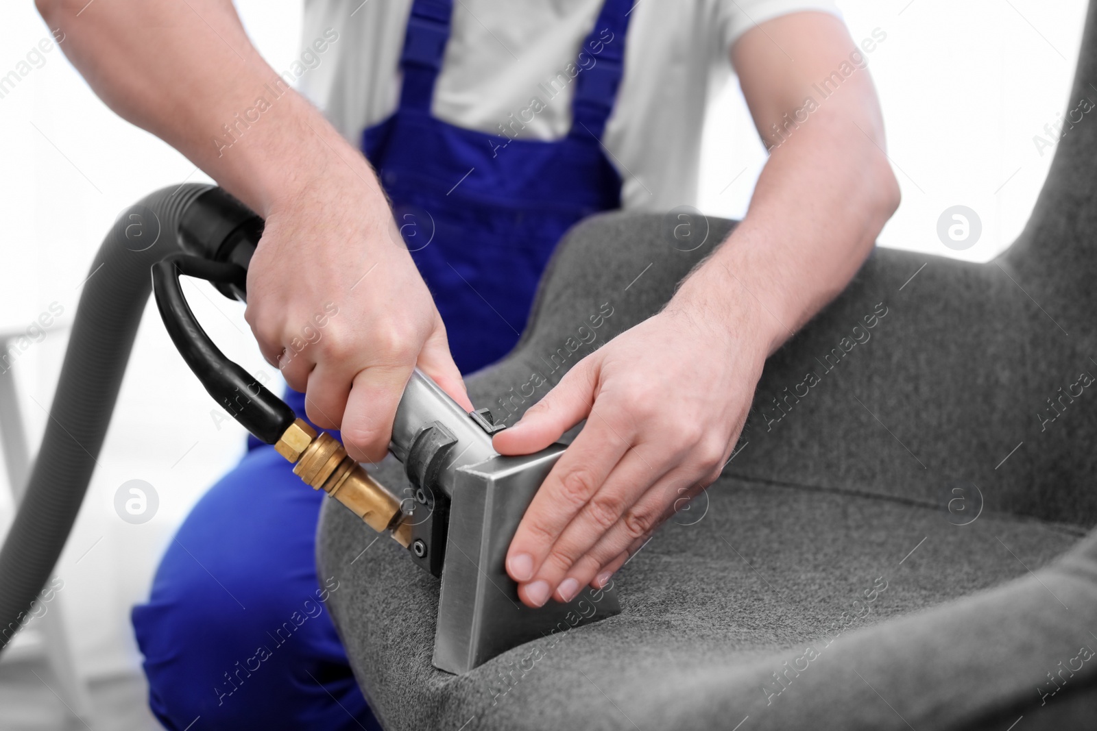 Photo of Dry cleaning worker removing dirt from armchair indoors