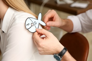 Photo of Man sticking paper fish to colleague's back in office, closeup. Funny joke