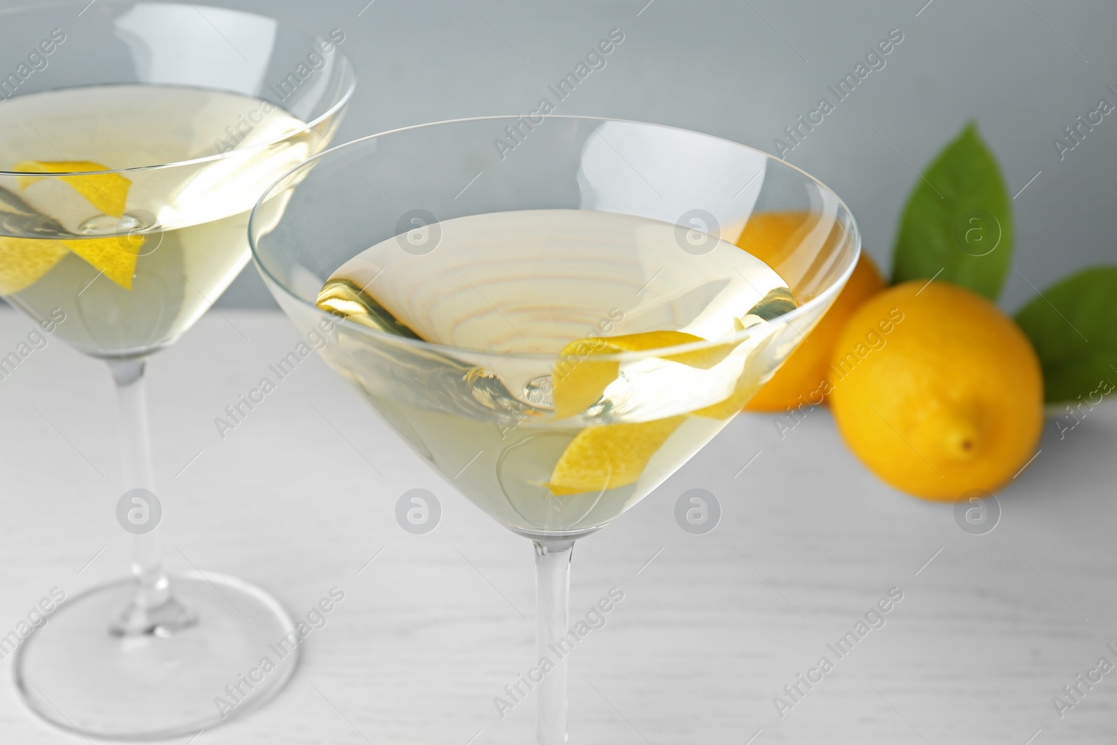 Photo of Glasses of lemon drop martini cocktail with zest on white wooden table against grey background