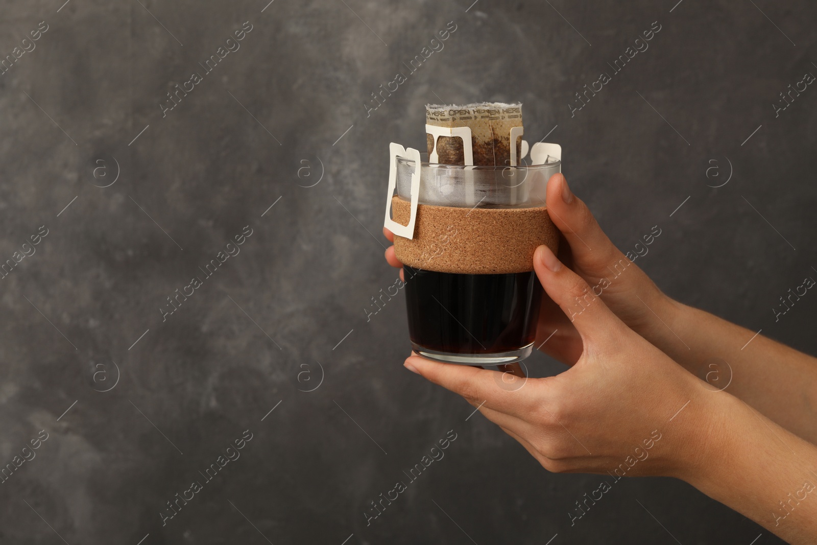 Photo of Woman holding cup with drip coffee bag on grey background, closeup. Space for text