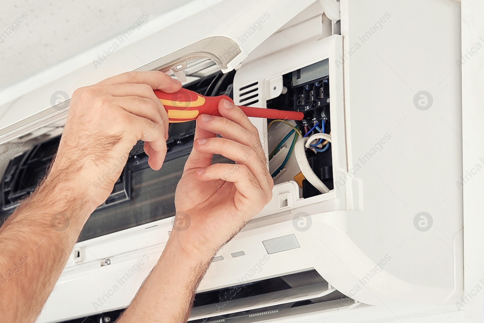 Image of Electrician with screwdriver fixing air conditioner indoors, closeup