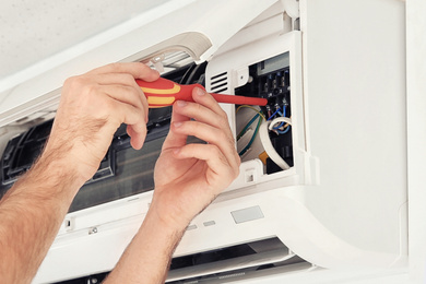 Image of Electrician with screwdriver fixing air conditioner indoors, closeup