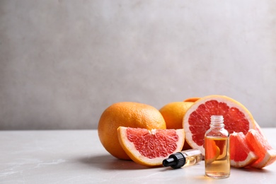 Bottle of essential oil and grapefruits on grey table, space for text