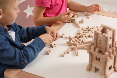 Photo of Little boy and girl playing with wooden tower at table indoors, closeup. Children's toy