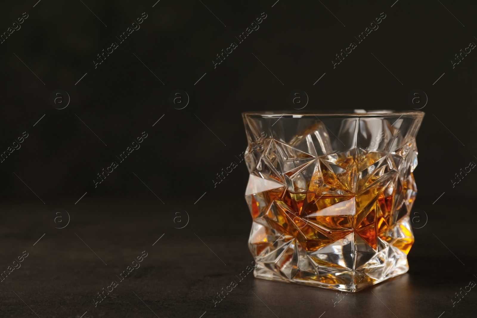 Photo of Golden whiskey in glass with ice cubes on table. Space for text