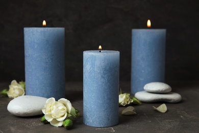 Burning candles, spa stones and flowers on dark grey table