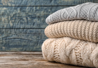 Stack of folded knitted sweaters on table. Space for text