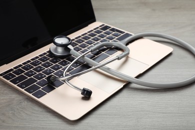 Laptop with stethoscope on wooden table, closeup