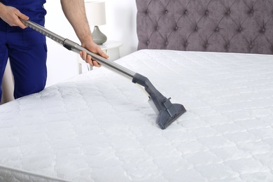 Photo of Man disinfecting mattress with vacuum cleaner, closeup