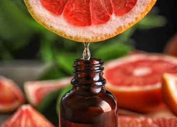 Photo of Citrus essential oil dripping from grapefruit slice into bottle, closeup