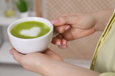 Woman with cup of delicious matcha latte indoors, closeup