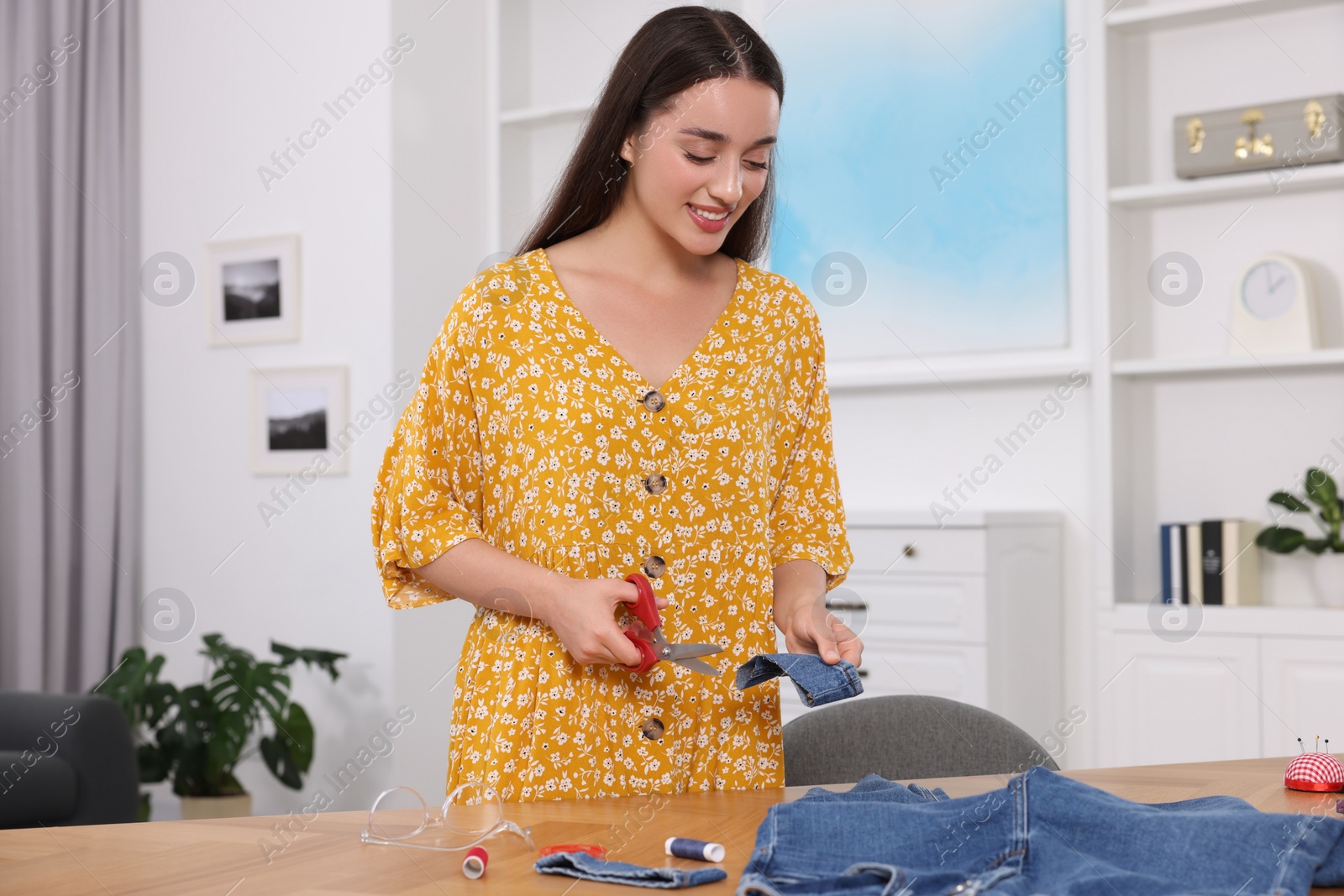 Photo of Happy woman holding cut hem and jeans at table indoors