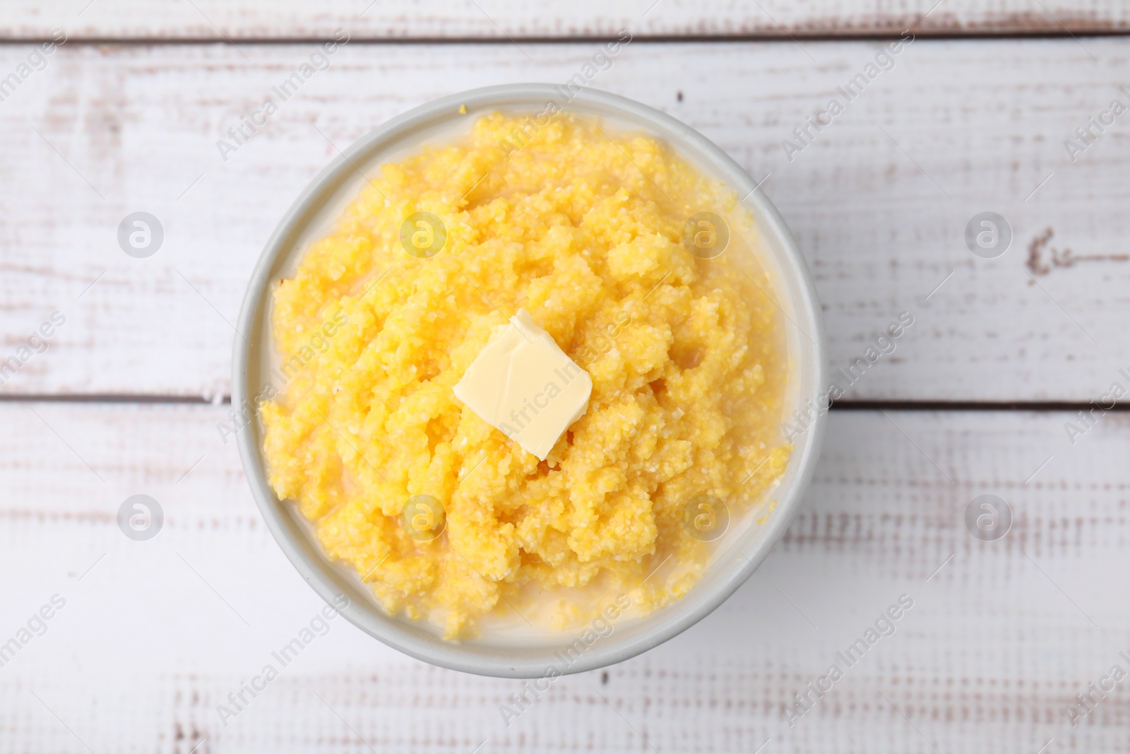 Photo of Tasty cornmeal with butter in bowl on white wooden table, top view