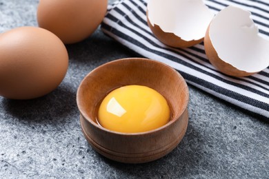 Raw chicken eggs and bowl with yolk on grey table, closeup