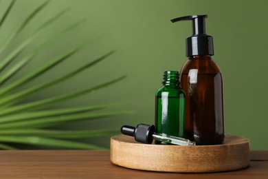 Photo of Bottles of hydrophilic oil on wooden table against green background. Space for text