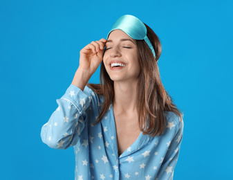 Beautiful woman wearing pajamas and sleep mask on light blue background. Bedtime