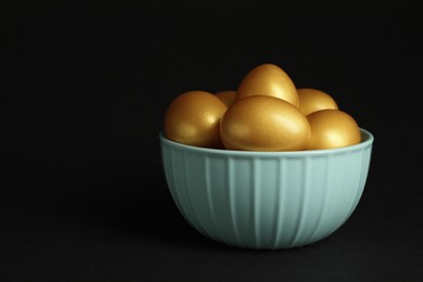 Shiny golden eggs in bowl on black background, space for text