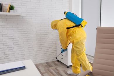 Photo of Janitor in protective suit disinfecting office to prevent spreading of COVID-19