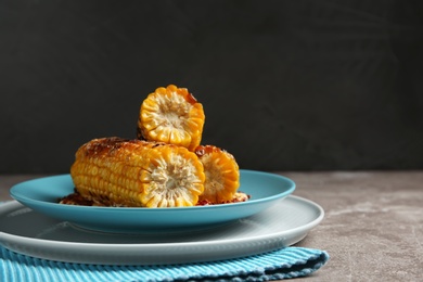 Plate with delicious grilled corn cobs and spices on table against gray background. Space for text