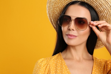 Beautiful woman wearing sunglasses on yellow background. Space for text